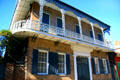 Brick house with upper cast-iron balcony & blue shutters. New Orleans, LA.