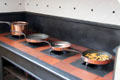 Copper pans with attached legs warming over heated grates in kitchen at St Fagans Castle. Cardiff, Wales.
