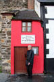 Visitor standing in front of The Smallest House in Great Britain to offer perspective on its size. Conwy, Wales.