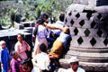Visitors try to touch Buddha covered by stone lacework stupa at Borobudur. Indonesia.