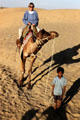 A little boy leads a tourist riding a camel across the Sam Sand Dunes. India.