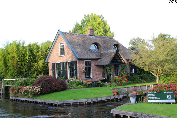 Home with ornate thatched roof broken with pair of windows on intersection of main & side canal. Giethoorn, Netherlands.