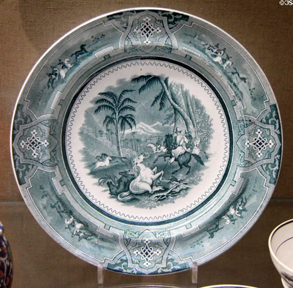 Underglaze-printed plate (1850-52) green with exotic hunting scene & Celtic interlace border made by Bristol Pottery at Bristol Museum & Art Gallery. Bristol, England.